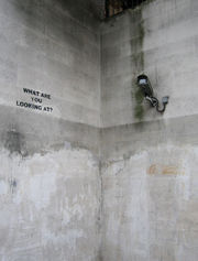 What are you looking at? — Graffito by Banksy commenting on the neighbouring surveillance camera in a concrete subway underpass near Hyde Park in London.