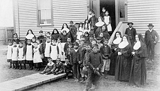 Photograph of female and male Aboriginal students, nuns and two men outside an Indian residential school, circa 1890