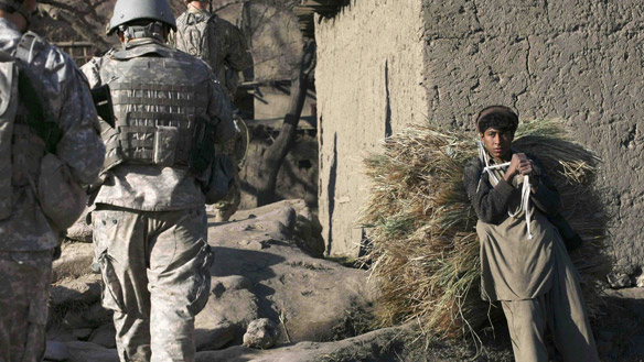 An Afghan youth carries a bundle of hay on his back as U.S. army soldiers pass by during a patrol in Kolack, a village in northeastern Afghanistan.