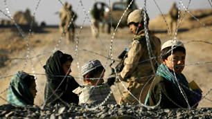 Afghan children look out from behind coils of razor wire as they watch Canadian troops and Afghan National Army soldiers patrol near the Mas'um Ghar base in the Kandahar province of Afghanistan in 2006.