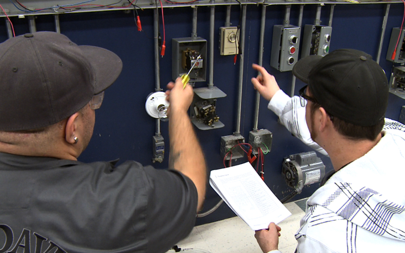 Étudiant de métier spécialisé examine un panneau circuit avec son instructeur