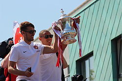 A coloured photograph of two men, footballers Aaron Ramsey and Kieran Gibbs, lifting a silver-coloured trophy, adorned with ribbons.