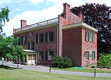 The rear of a classic, red-brick building with beige trim is shown beyond a driveway.