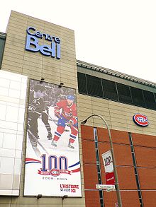 Façade of the Bell Centre. On the wall is a banner celebrating the Canadiens centennial, featuring two players, one in black and white and one in color, and the Canadiens logo in front of a "100".