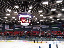 A brightly lit hockey arena, panning upward to show a sloped ceiling and a large, cylindrical television screen.