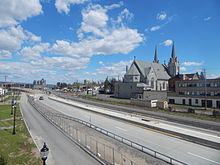 A highway, under construction, runs across the photo from top left to bottom right. Next to the highway is a large church and some buildings on the right.