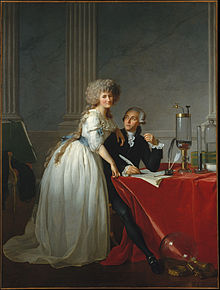 Full-length portraits of a man and a woman. The man is seated at a table covered with a bright red cloth, looking up at the woman, and she is looking out at the viewer. They occupy the bottom half of the painting, while the top half resembles marble and pillars. She is wearing a white dress with a blue sash and he is wearing a dark coloured suit. Glass chemistry equipment sits on the table and on the floor.