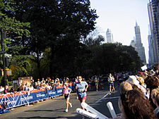 Three runners in a race down a street where onlookers are cheering behind barriers.