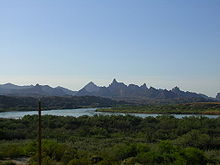 View of a wide river flowing through a forested area, with jagged mountains in the background