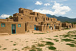 A cluster of reddish brown small adobe houses with blue doors and window frames.