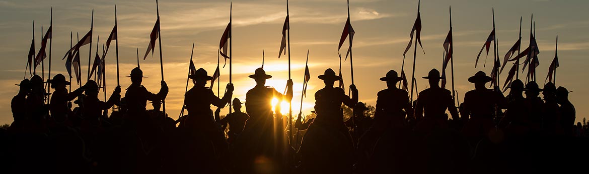 A silhouette of Musical Ride members on horseback with sunset in background