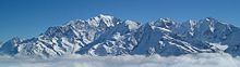 panorama of Mont Blanc mountain range above gray clouds under a blue sky