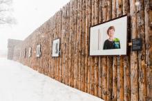 Frames are hung on a stockade wall. The first frame shows the portrait of a smiling woman.