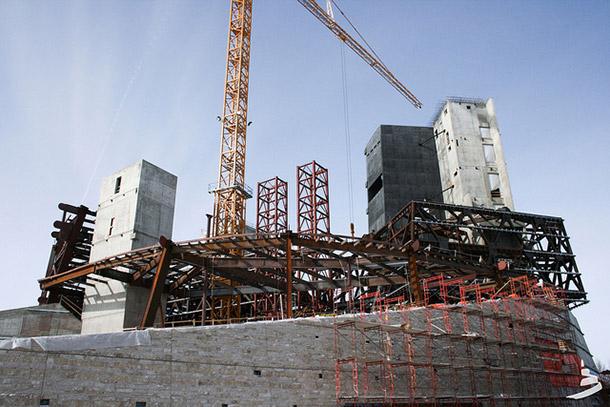 Construction site of the Canadian Museum for Human Rights, with iron scaffolding, the beginnings of a concrete façade, and a tall crane visible.