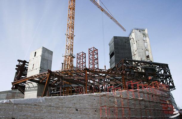 Construction site of the Canadian Museum for Human Rights, with iron scaffolding, the beginnings of a concrete façade, and a tall crane visible.