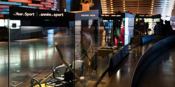 A row of display cases in a museum gallery. The first case displays text that reads &quot;The Year of Sport&quot;.