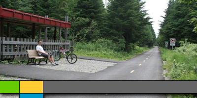 Un cycliste assis sur un banc sous un auvent rouge à côté de la piste cyclable nouvellement pavée