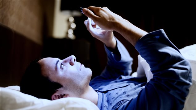 Un homme consulte son téléphone dans son lit.