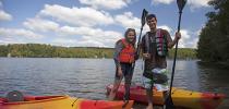 Photo of two people standing next to their kayaks on a Gatineau Park lakeshore