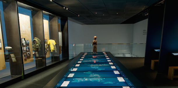 A large digital media table in the middle on a gallery, a statue standing in the back