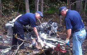 Two TSB investigators examining aircraft wreckage in a wooded area