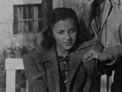 A girl wearing a coat sits on a bench in a black and white photo.