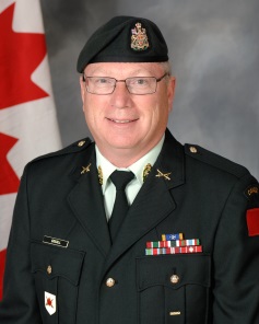 A soldier poses for a formal photo in front of the Canadian flag.