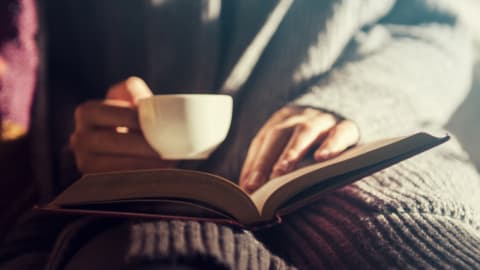 Une femme lit un livre en tenant une tasse de café. 