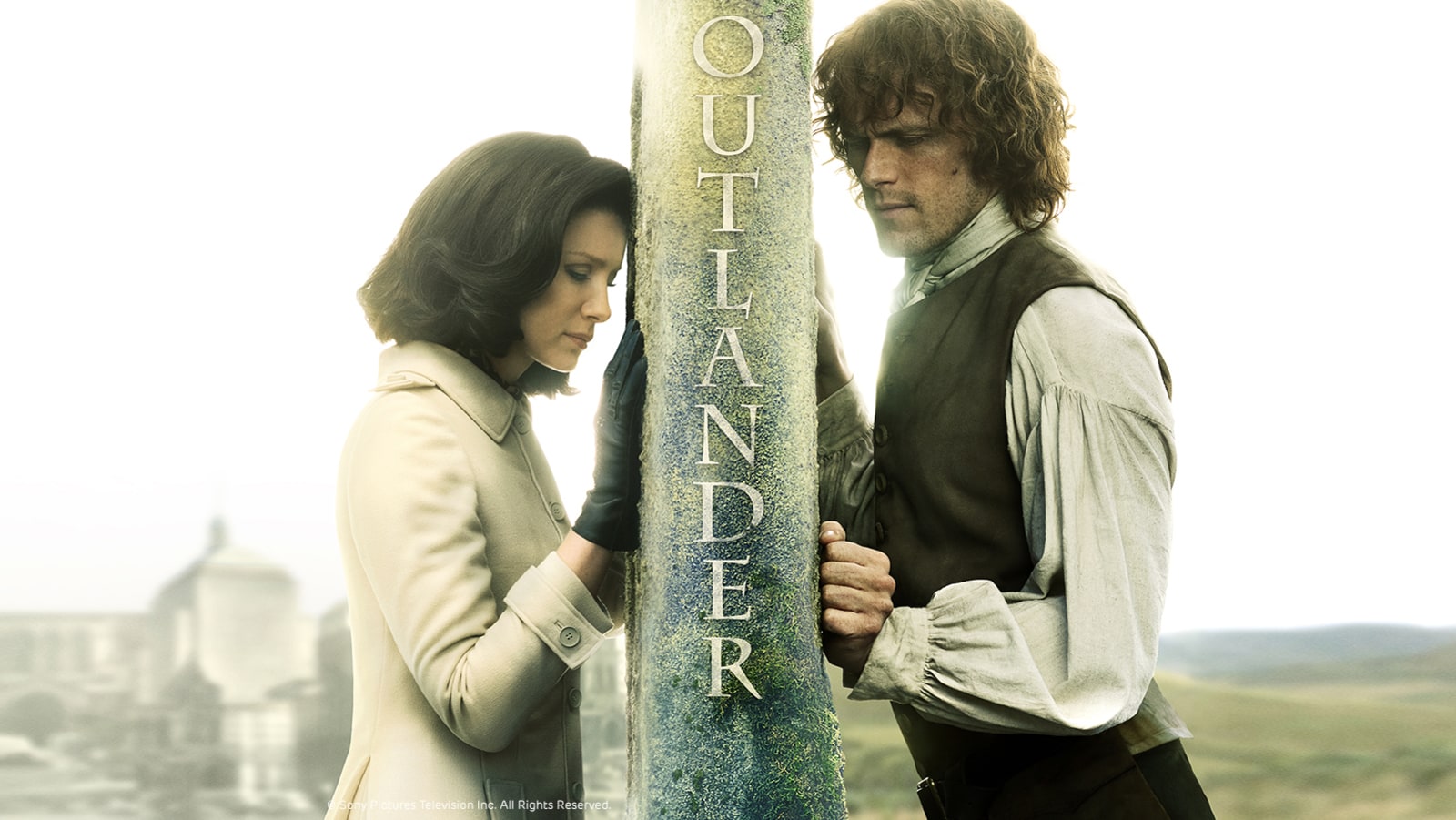 Les deux personnages principaux de la série Outlander, Claire et Jamie, séparés par un mur de pierre qui rappelle leur éloignement temporel.