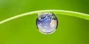 A drop of water with Earth superimposed on it, hanging from a blade of grass.
