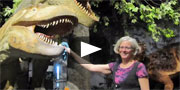 A woman poses with cleaning products beside a life-sized model of Daspletosaurus torosus.