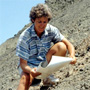 Kathy Stewart crouches on a steep, rocky slope while consulting a large sheet of paper.