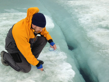 A man crouches on sea ice.