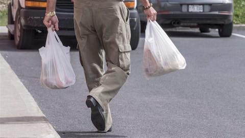 Un homme transporte ses emplettes dans des sacs en plastique.