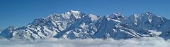 Panorama of Mont Blanc mountain range above gray clouds under a blue sky