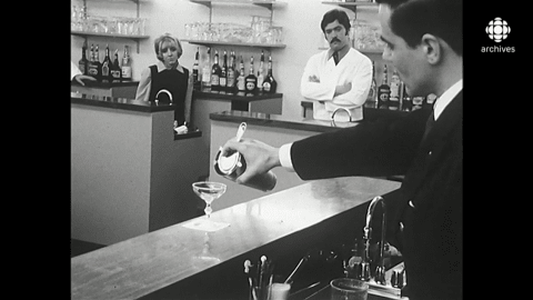 Un enseignant prépare un cocktail Gimlet à l'aide d'un shaker devant une classe d'étudiants derrière leurs bars respectifs.