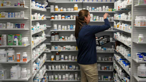 Une employée d'une pharmacie dépose des médicaments sur des tablettes.