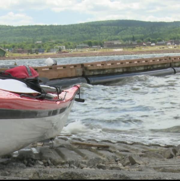 On voit un kayak de très près. Il est en bordure d'un plan d'eau, près de quai. 