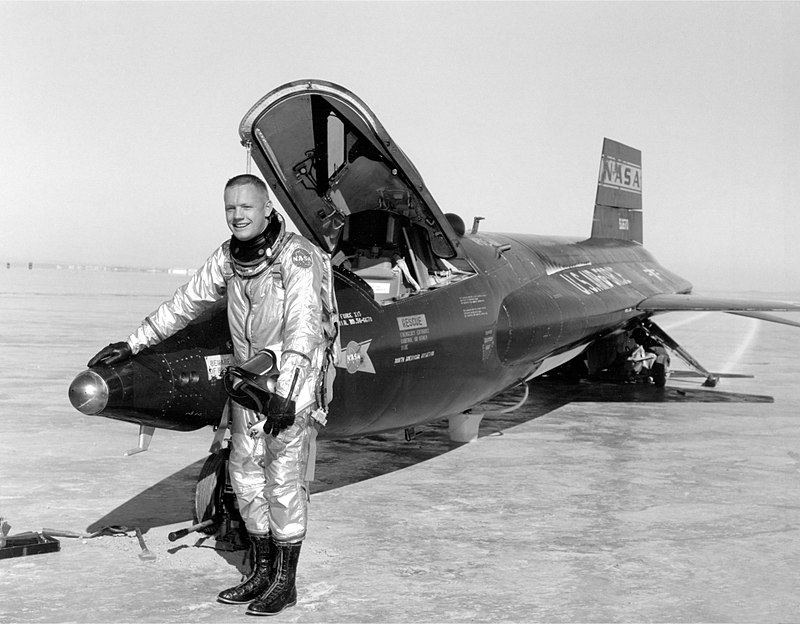 Black-and-white 1960 photograph of Neil Armstrong smiling in a NASA suit and resting his right hand on the tip of an X-15 aircraft
