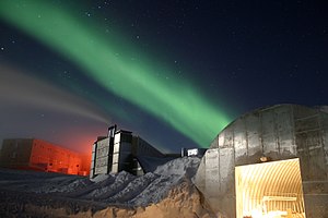 Retouched photograph of Amundsen–Scott Station in Antarctica with a greenish Aurora Australis streaking across the clear night sky