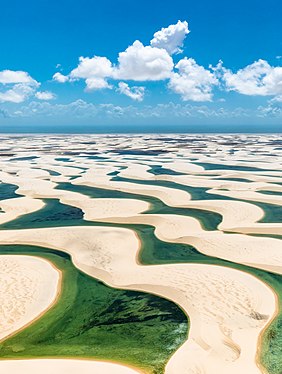 Photograph of the Lençóis Maranhenses National Park depicting fresh water collecting in the valleys between sand dunes, a layer of rock beneath the sand preventing the rain water from dissipating during the rainy season, thus resulting in a broad expanse of lagoons