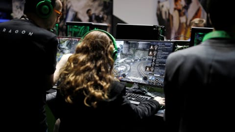 Un visiteur aux cheveux blonds assis de dos joue à un jeux vidéo.