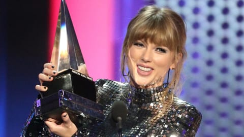 Taylor Swift brandit un trophée dans ses mains devant un micro sur scène
