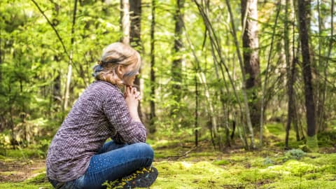 Une femme assise par terre, qui fait de la méditation en forêt.