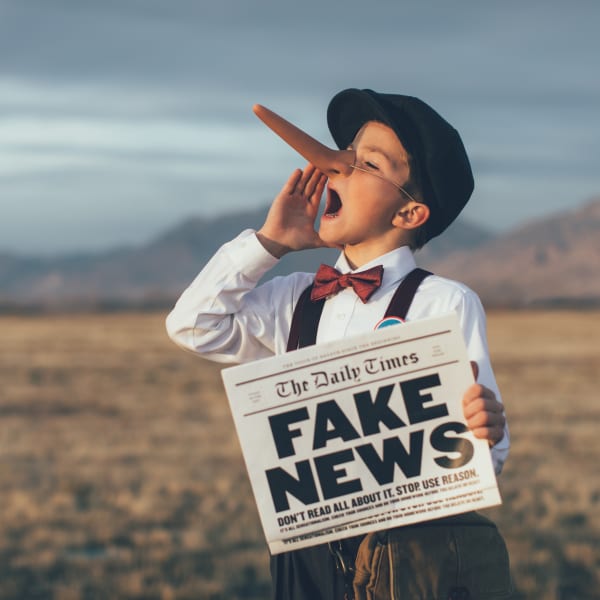 Un garçon, vêtu de vêtements d'antan, tient un journal en main sur lequel on peut lire «fake news». Il porte aussi un pastiche sur le nez qui rappelle Pinocchio.