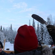 Un manifestant tient une plume dans la main droite devant des policiers, dans une forêt recouverte de neige. 