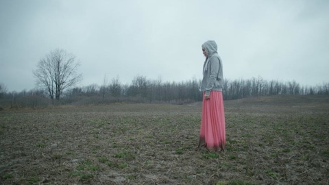 Une femme avec une robe rose est debout dans un champ gris et terne.