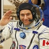 L'astronaute David Saint-Jacques en habit, devant une photo de la Terre vue de l'espace.