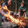 Un père et son fils devant un feu de camp. Le jeune se réchauffe les mains pendant que son père alimente le brasier. 