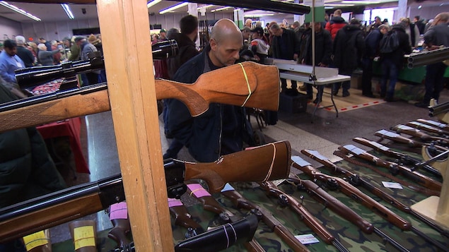 Un homme examine des fusils étalés sur une table lors d'un salon pour amateurs d'armes à feu à Longueuil.